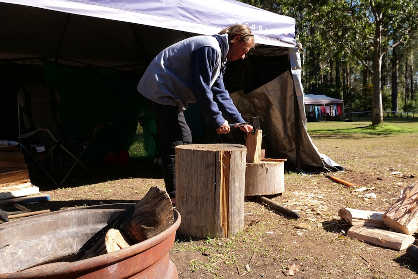 Man cutting wood outside his camping annex 