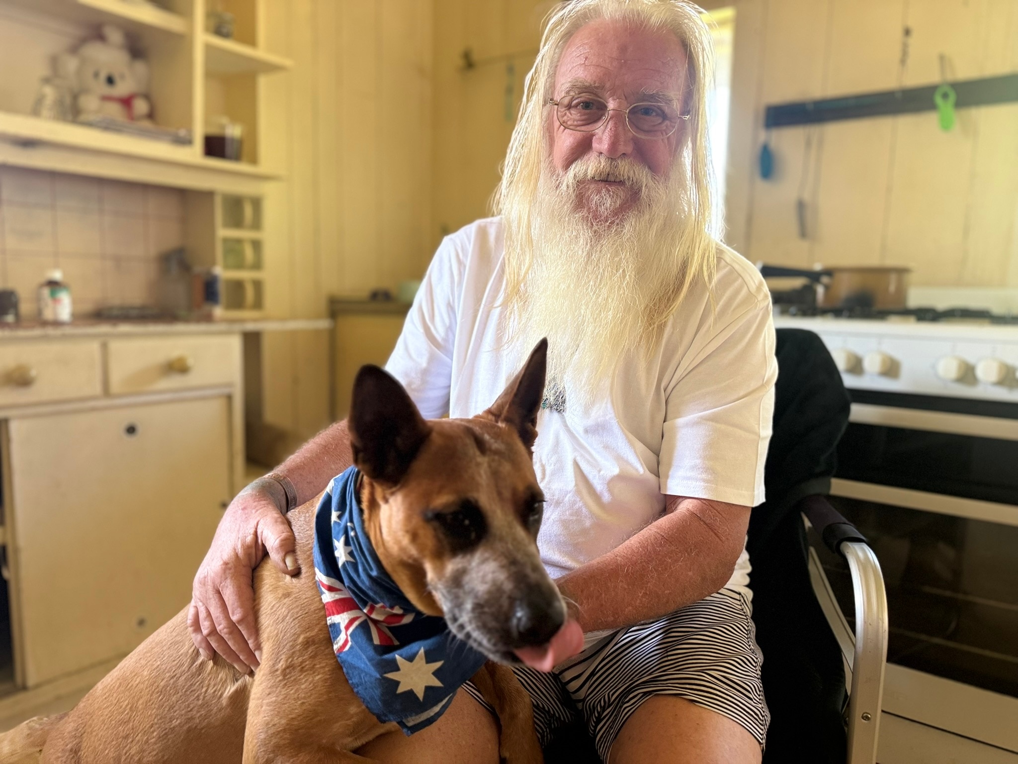 Man with white hair and beard with a white shirt with a dog.