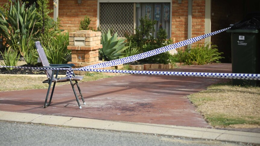 Police tape tied to a chair on a driveway with blood spatters out the front of a suburban house.