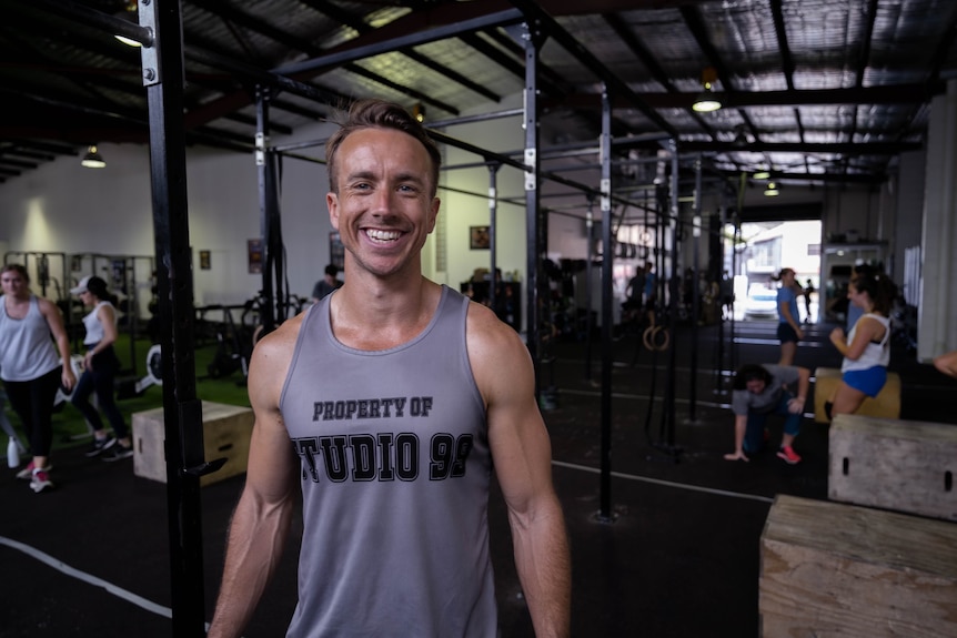 Tim stands smiling in the middle of the gym, where people workout in the background