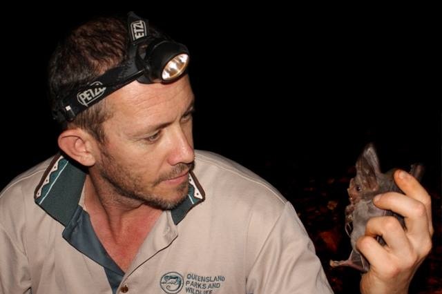 A man with a head torch looks at a small creature in his hand.