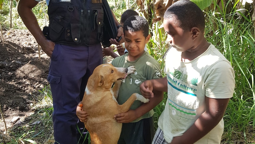 A police officer stands with two boys whose dog is jumping up on them. 