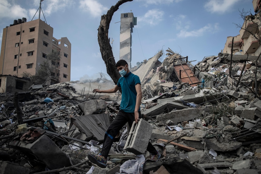 A Palestinian man inspects the rubble from a six-story building destroyed by air strikes.