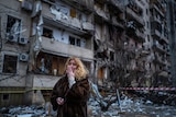 A crying woman stands outside a badly damaged residential tower