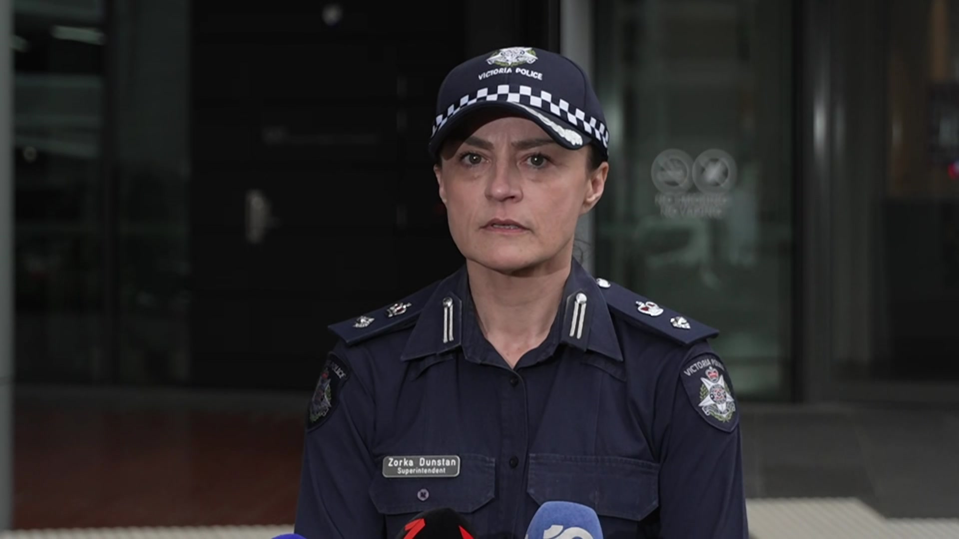 A dark haired woman wearing a navy police cap and police uniform stares at the camera.
