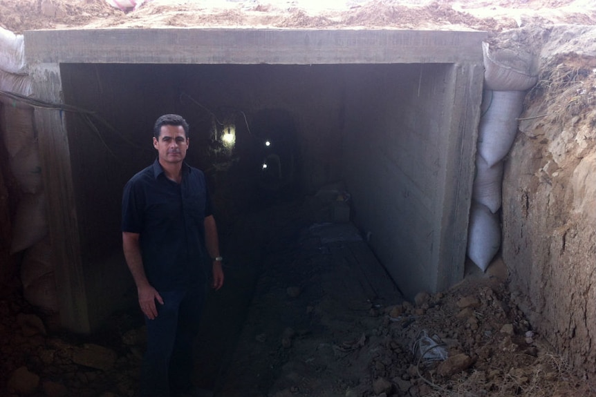 Brown standing at entrance to tunnel carved into rock.