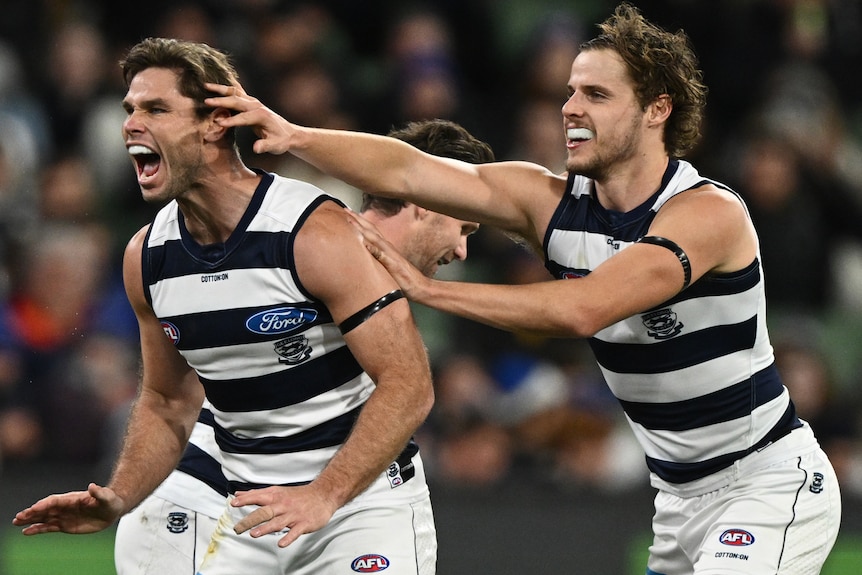 Two Geelong AFL players dressed in black and white jersey, white shots, one has hand on the head and shoulder of another.