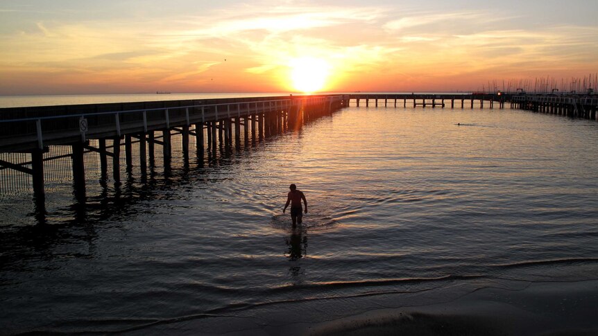 At sunset, a sole swimmer emerges from the water at the Brighton sea baths in Melbourne.