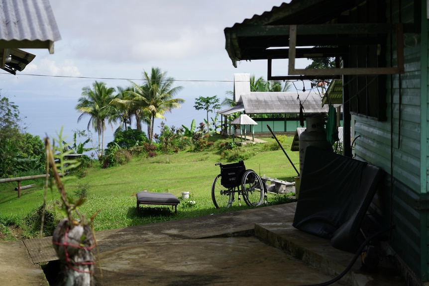 Bits of hospital equipment including a wheelchair and old mattress sit in between two weatherboard buildings, looking out to sea