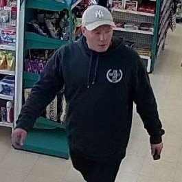 A man wearing a cap, black clothing and red shoes walking inside a store.