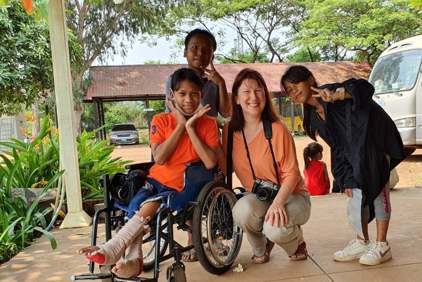 A woman squatting next to a child in a wheelchair with an injured leg with two other children and a dog