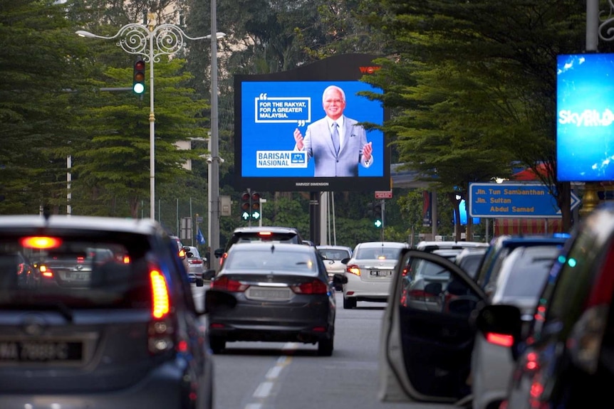 Cars drive in front of a billboard promoting Malaysian PM