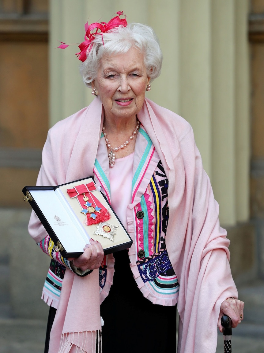 A woman wearing a light pink shawl displays an award.