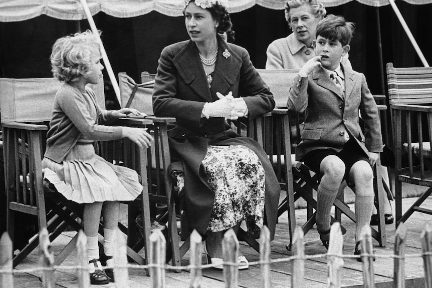 Queen Elizabeth II sits between her children, Princess Anne and Prince Charles, as they watch a polo match