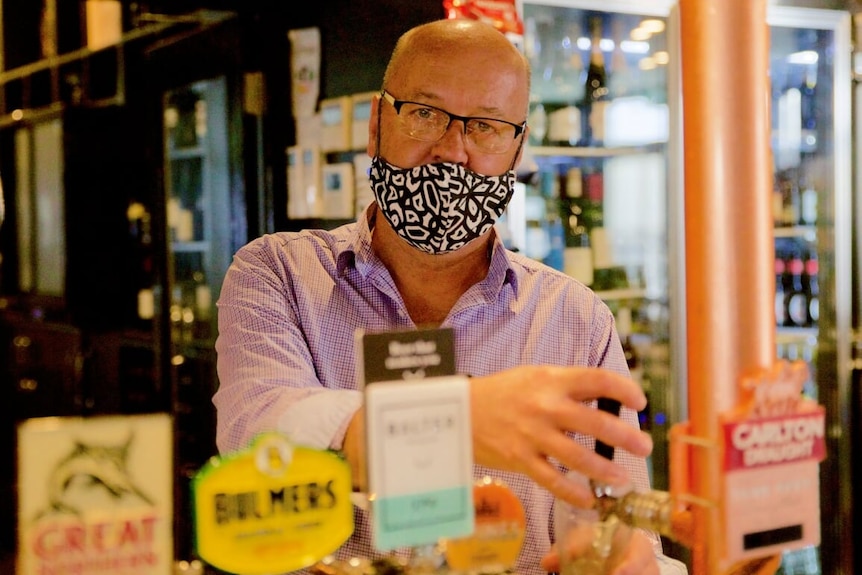 A man in a mask pulling a beer behind a bar.