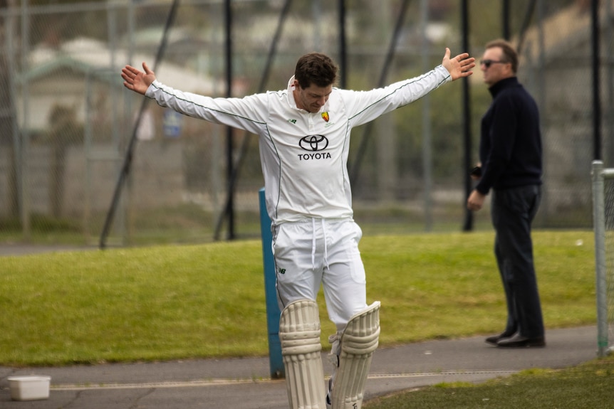 クリケット選手のティム・ペインは、白い服を着て腕を大きく広げてネットに立っています。 