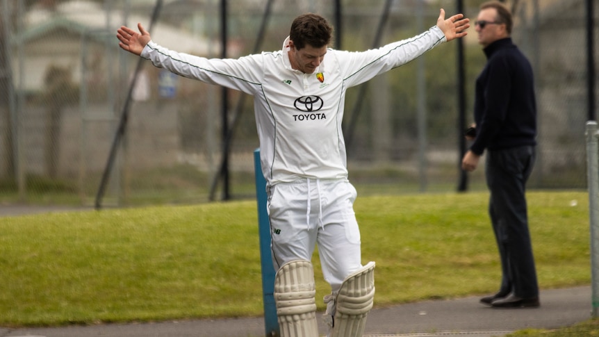 Cricketer Tim Paine stands in the nets holding his arms out wide  dressed in whites. 