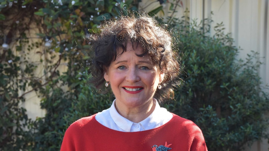 Maree White, a woman with curly brown hair and a red jumper, smiles calmly at the camera.