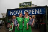 Two women holding babies stand outside a shop.