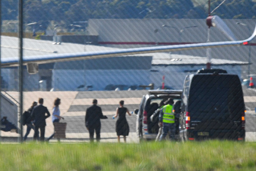 A group of people appear to usher a woman from a plane into a black car