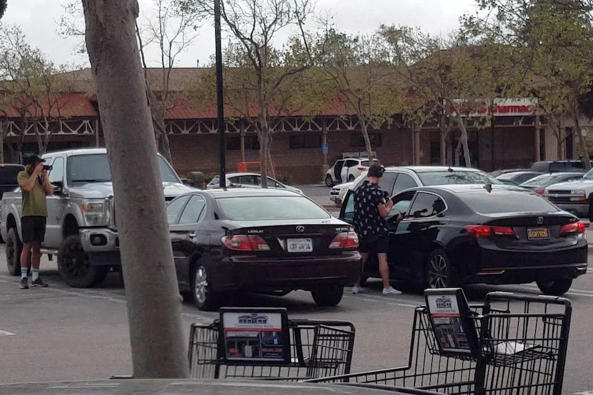 A wide angle shot of people standing outside a black car.