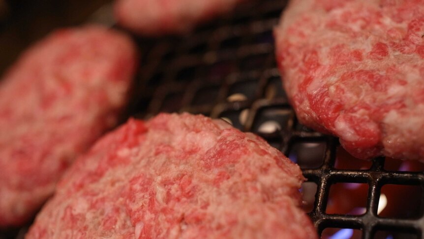 close up of three meat patties on a grill