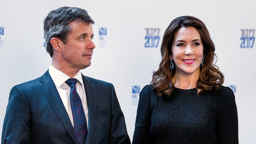 Prince Frederik and Princess Mary pose in front of a white wall and smile at the press.