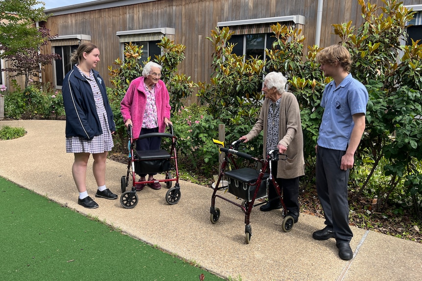 Two students having a conversation with two aged care residents in a courtyard.