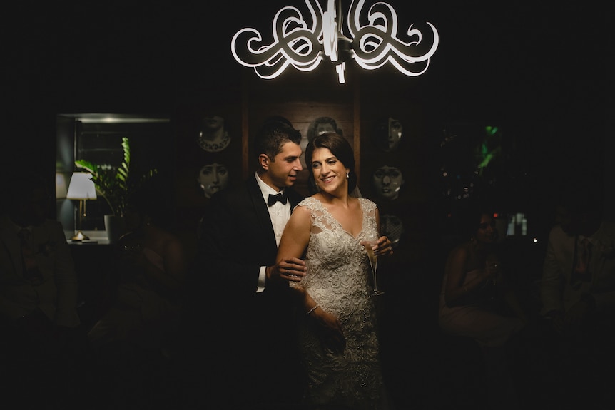Artistic intimate photo of a couple just married holding drinks at a dark indoor venue.