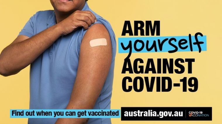 A man lifts his sleeve to show where he has been vaccinated. Poster reads "arm yourself against COVID-19".