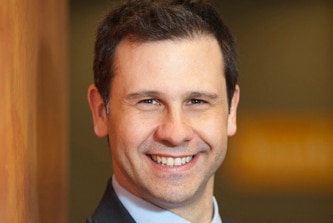 A man with dark hair who is dressed in a shoot smiles for the camera.