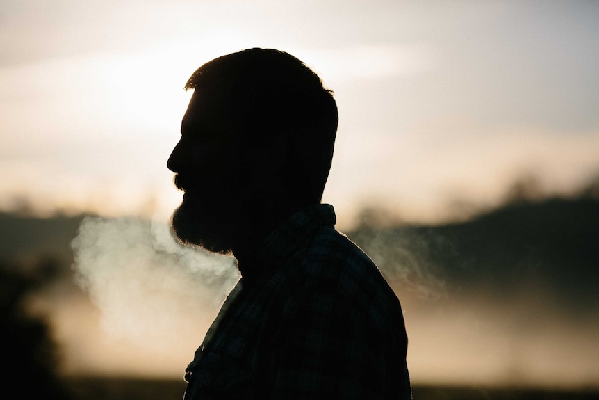 A man with a beard stands in a shadow.