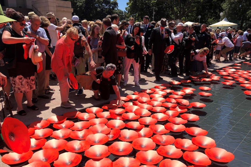A group of people place poppies on a water feature at the Anzac Memorial water feature.