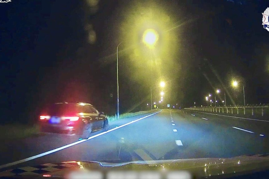 A police car following an Audi on the highway at night.