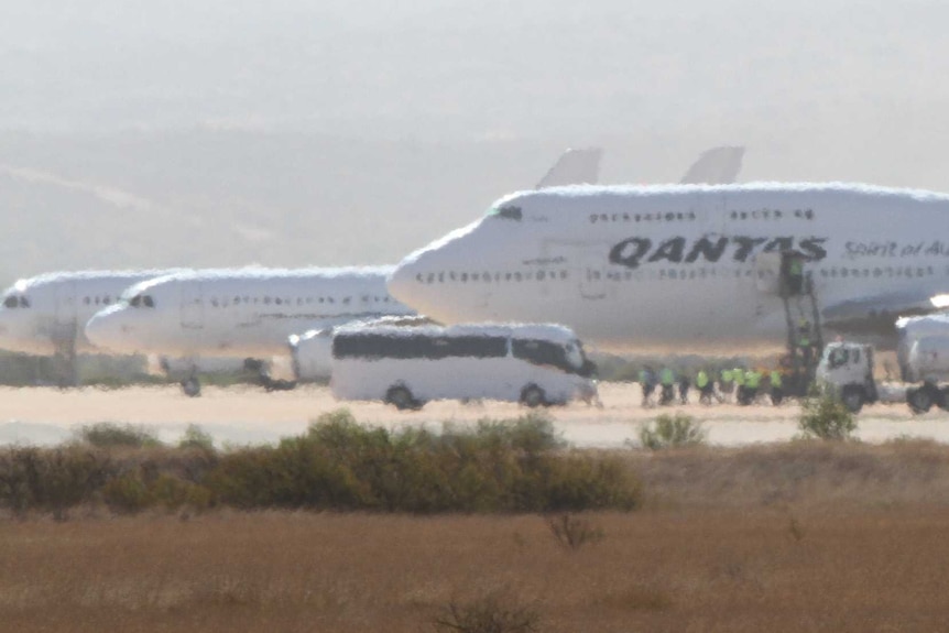 A Qantas plane next to two smaller planes on a remote airstrip.