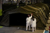 Army tents are set up in an underground carpark as medical staff in white inspect them.
