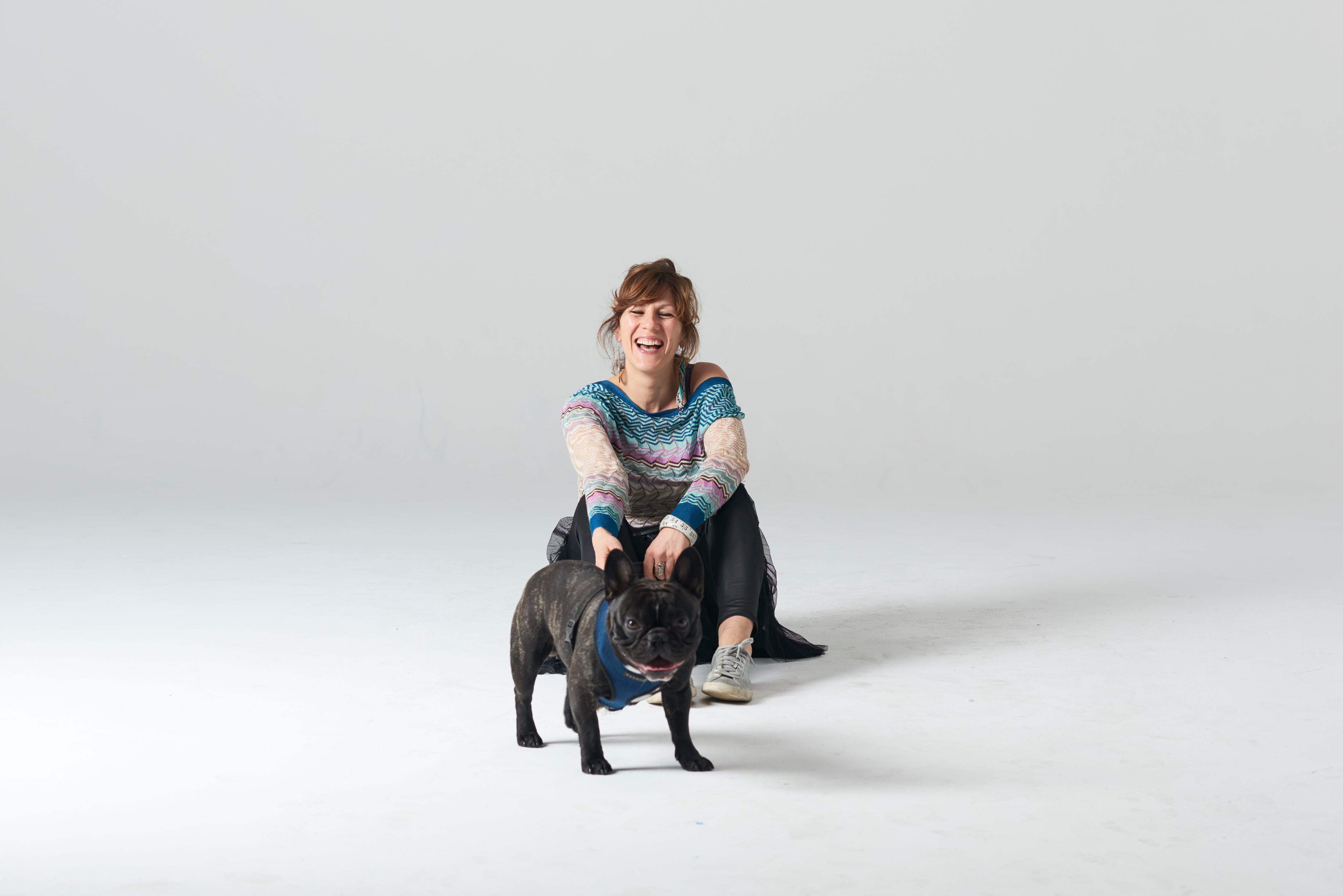 Portrait of Tamara DiMattina laughing and holding a French bulldog in a white room