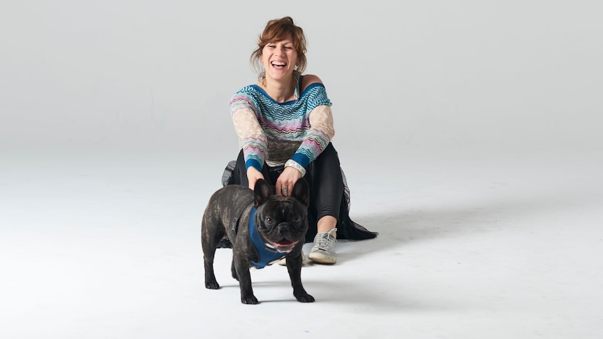 Portrait of Tamara DiMattina laughing and holding a French bulldog in a white room