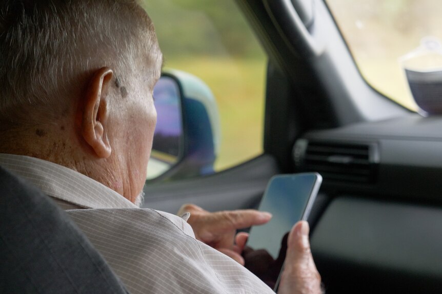 Kevin Waters on a smartphone in a car, St George, Queensland, March 2024.