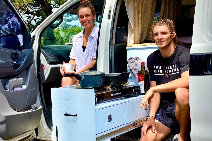 Woman and a man sitting in a van on the beach.