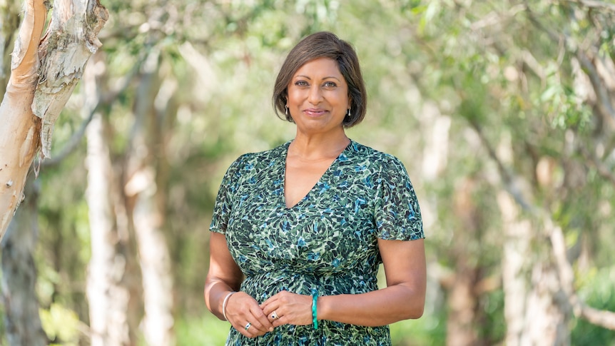 Woman wearing a green floral dress standing in the middle of a thick row of treesl