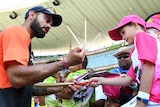 Virat Kohli, in his training gear, signs an autograph on a mini bat for a young Australian fan.