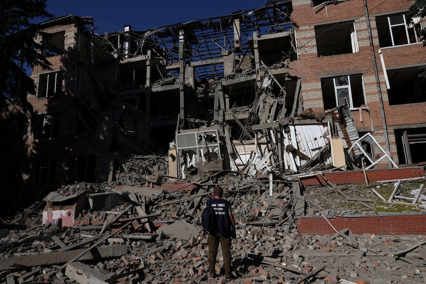 A man stands in front of apartment wreckage in Ukraine