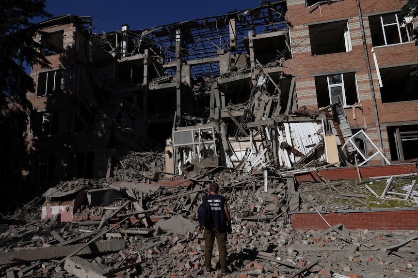 A man stands in front of apartment rubbble in Ukraine