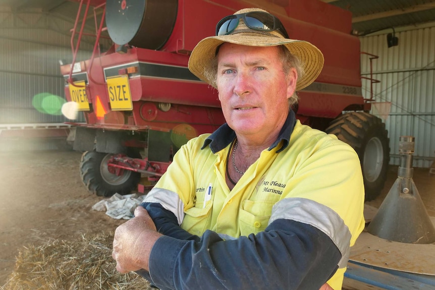 Farmer Martin Honner, wearing a high-vis work top, stands with his arms folded near machinery in a shed.