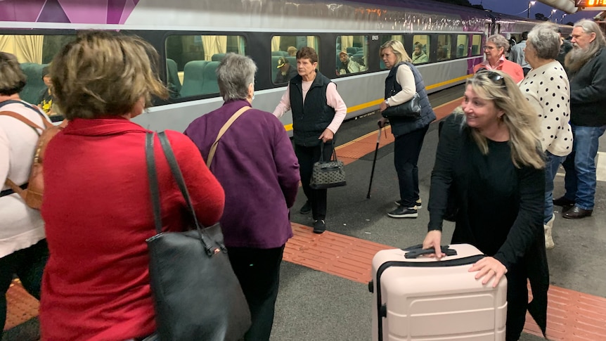 a crowd of people board a train at an outdoor platform.