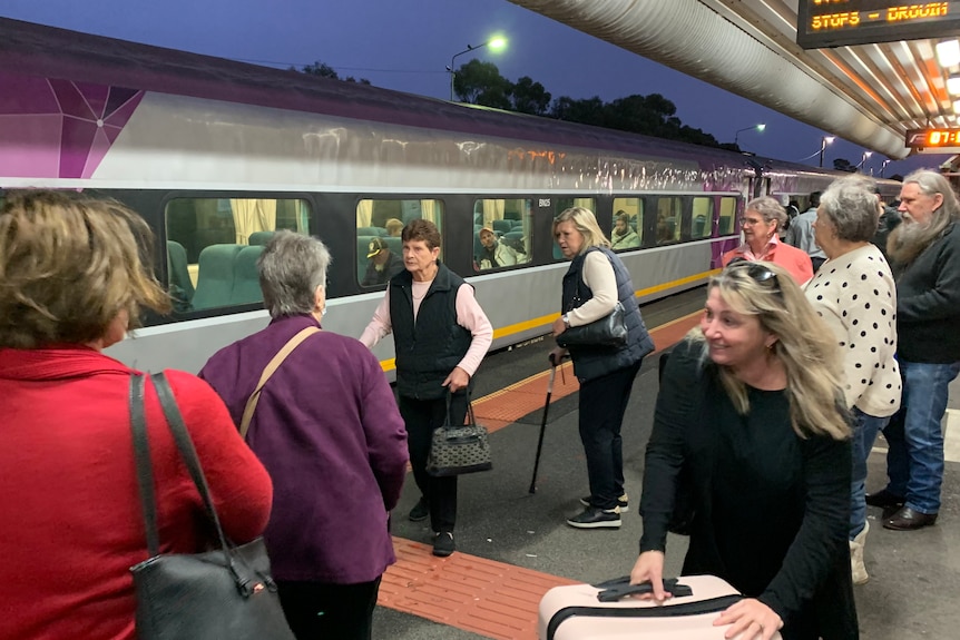 a crowd of people board a train at an outdoor platform.