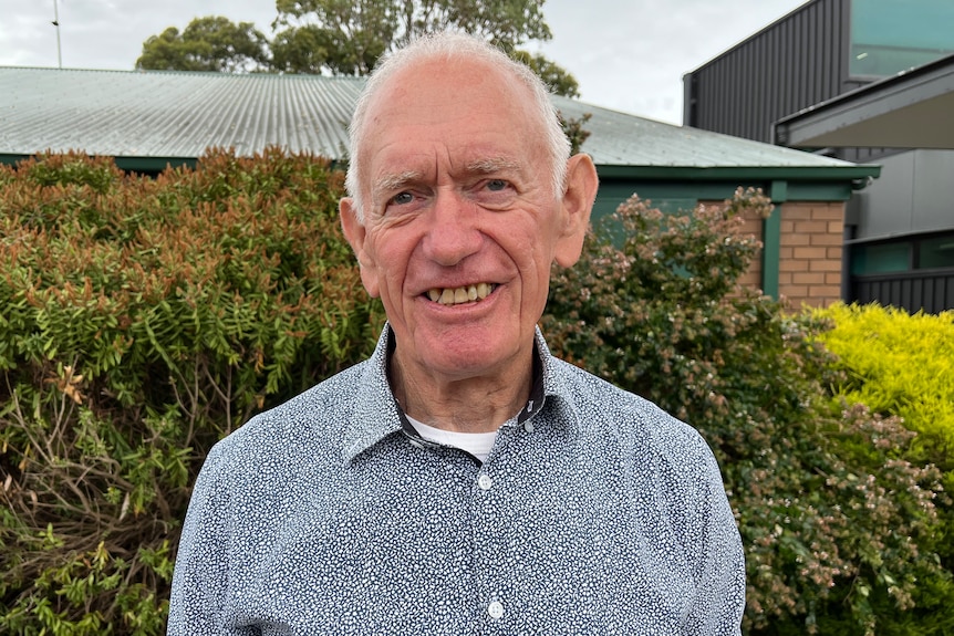 a man with short gray hair smiles at the camera outside.