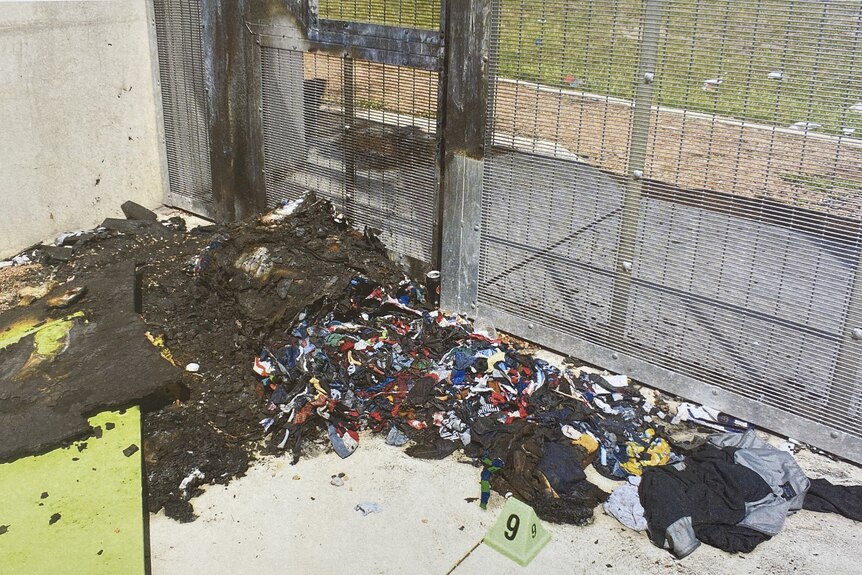 Fire damage and piled up clothes in an outdoor area of a prison.