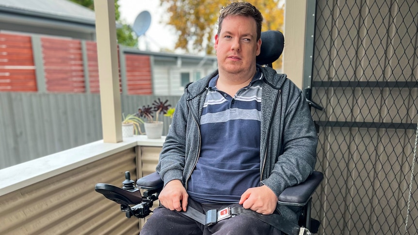 A man in a blue jumper sitting outside in a wheelchair